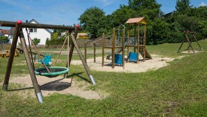Un parque infantil con columpios, una estructura para escalar y un pequeño refugio.