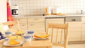Una cocina con armarios de madera, microondas y lavavajillas. Hay una mesa de comedor con sillas y un cojín de colores.