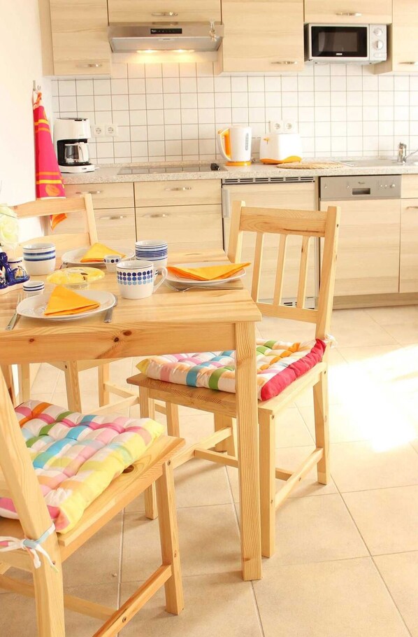 A kitchen with wooden cabinets, a microwave, and a dishwasher. There is a dining table with chairs and a colorful cushion.