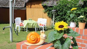 Un jardín con una escultura de caracol, un girasol y un edificio con techo de paja.
