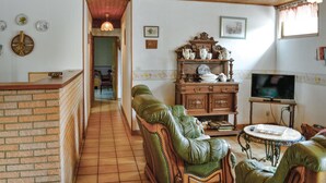 A cozy living room with a brick fireplace, green leather chairs, a wooden cabinet with decorative items, and a television on a wooden stand.
