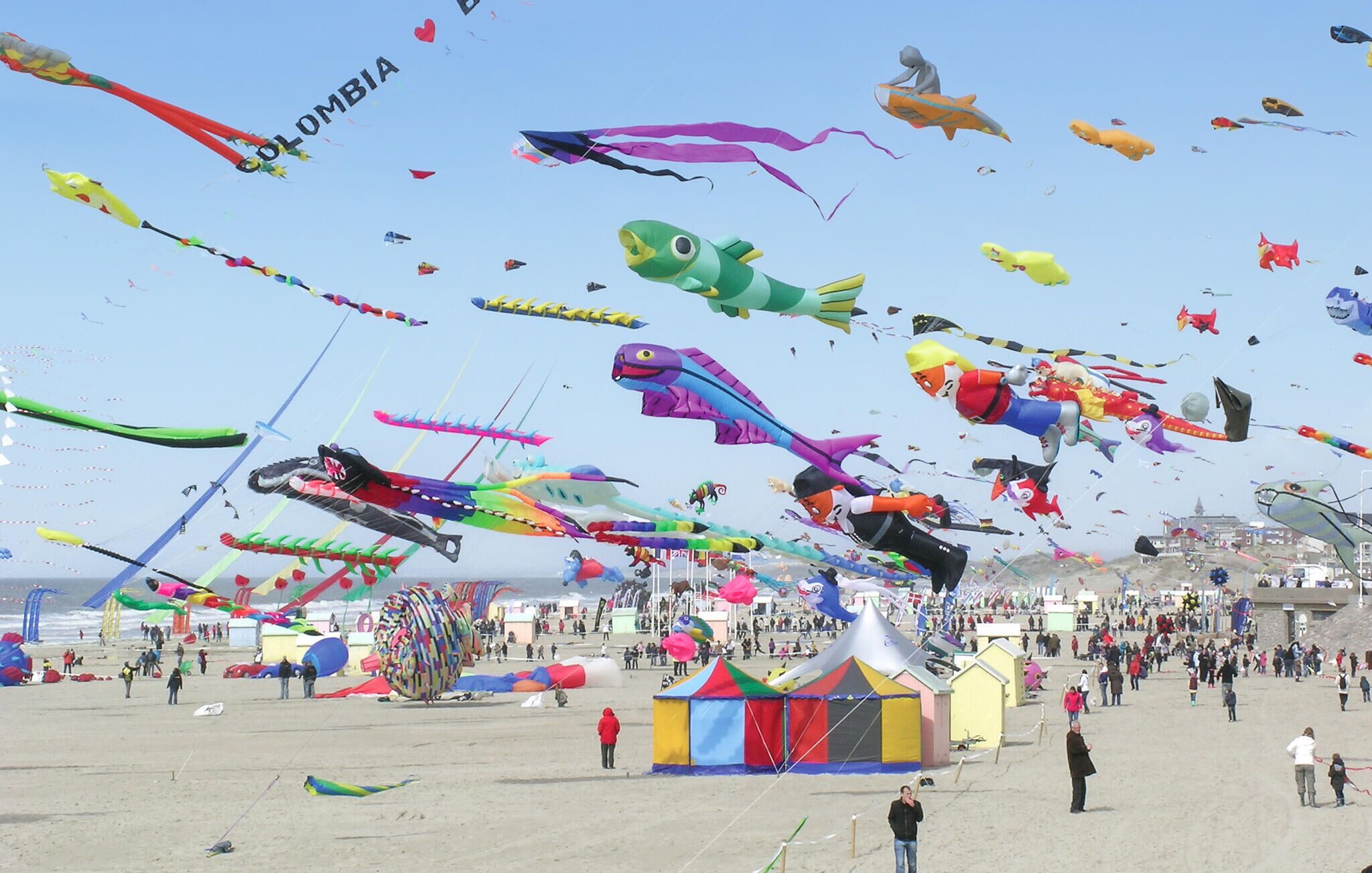 A beach with numerous colorful kites and tents.