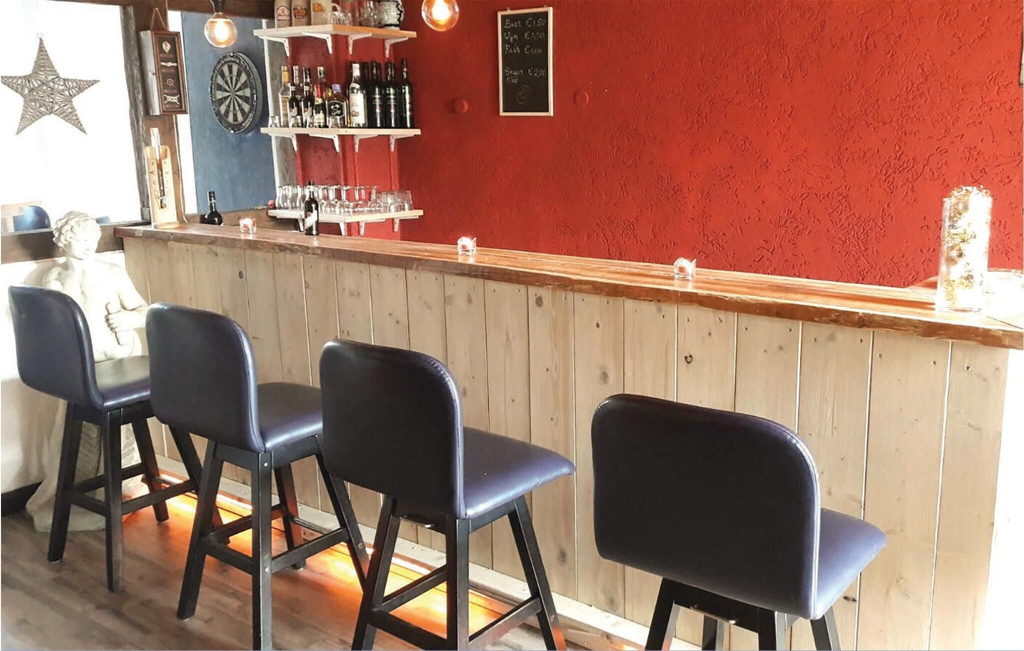 Zona de bar con mostrador de madera, taburetes negros y estantes con botellas y copas.
