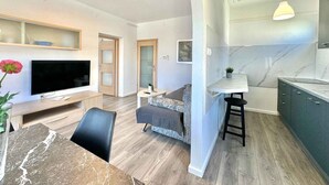 Uma sala de estar moderna com televisão de tela plana, uma mesa de jantar, um sofá e uma área de cozinha com bancada de mármore.