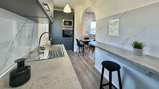 Uma cozinha moderna com bancada de mármore, eletrodomésticos de aço inoxidável e vista para o exterior.