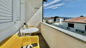 Uma varanda com mesa e cadeiras, com vista para uma área residencial com edifícios e céu claro.