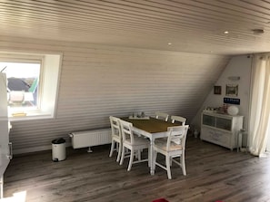 Un coin repas avec une table en bois et des chaises blanches, un radiateur, une poubelle et un meuble sur lequel on peut voir une étiquette de whisky.