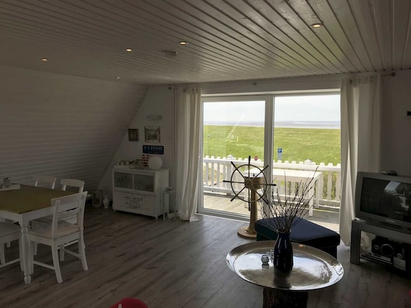 Une pièce comprenant une table à manger, des chaises, un téléviseur et une grande fenêtre donnant sur la mer.
