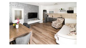 Ein modernes Wohnzimmer mit Esstisch aus Holz, einer Couch und einem Fernseher.