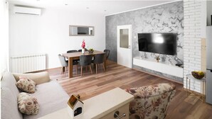 A modern living room with a sofa, a dining table, and a TV mounted on a marble wall.
