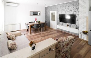 A modern living room with a sofa, a dining table, and a TV mounted on a marble wall.