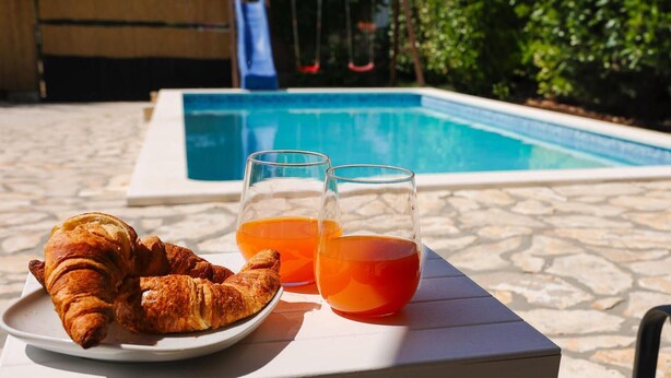 Ein Poolbereich mit einem Teller Croissants und zwei Gläser Orangensaft.