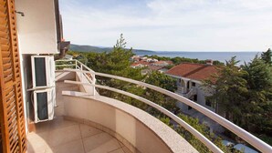 Varanda com guarda-corpo curvo com vista para uma vila costeira, um persiana de madeira e um aparelho de ar condicionado.