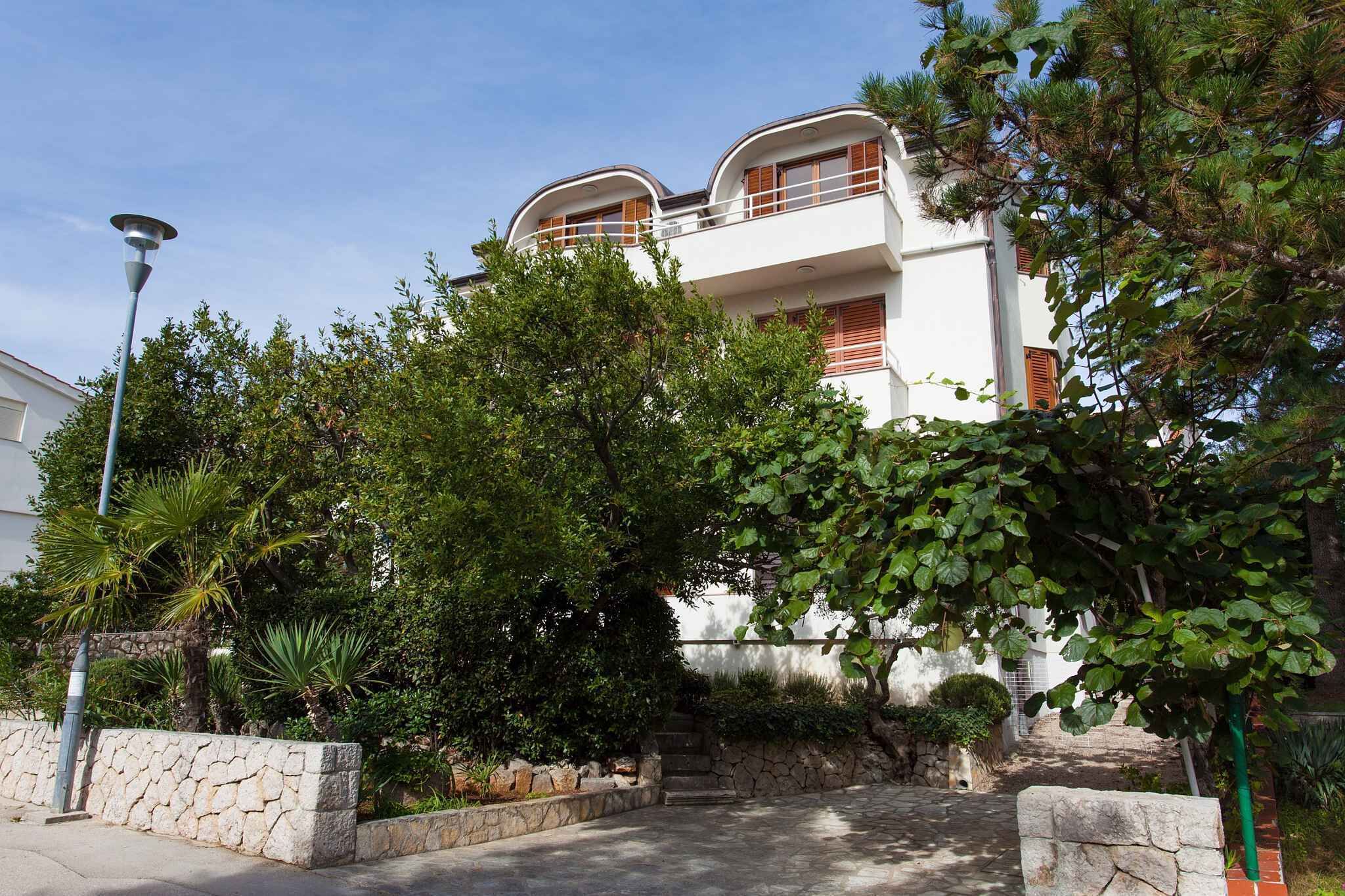 A two-story building with a white facade, wooden balconies, and a stone wall in the foreground.