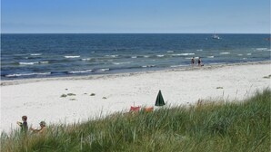 Uma praia com areia branca, um guarda-sol verde e um veleiro ao longe.