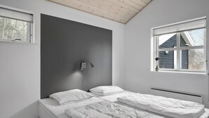 Quarto minimalista com uma cama de solteiro, mesa de cabeceira, luminária fixada na parede e janela com vista para o exterior.
