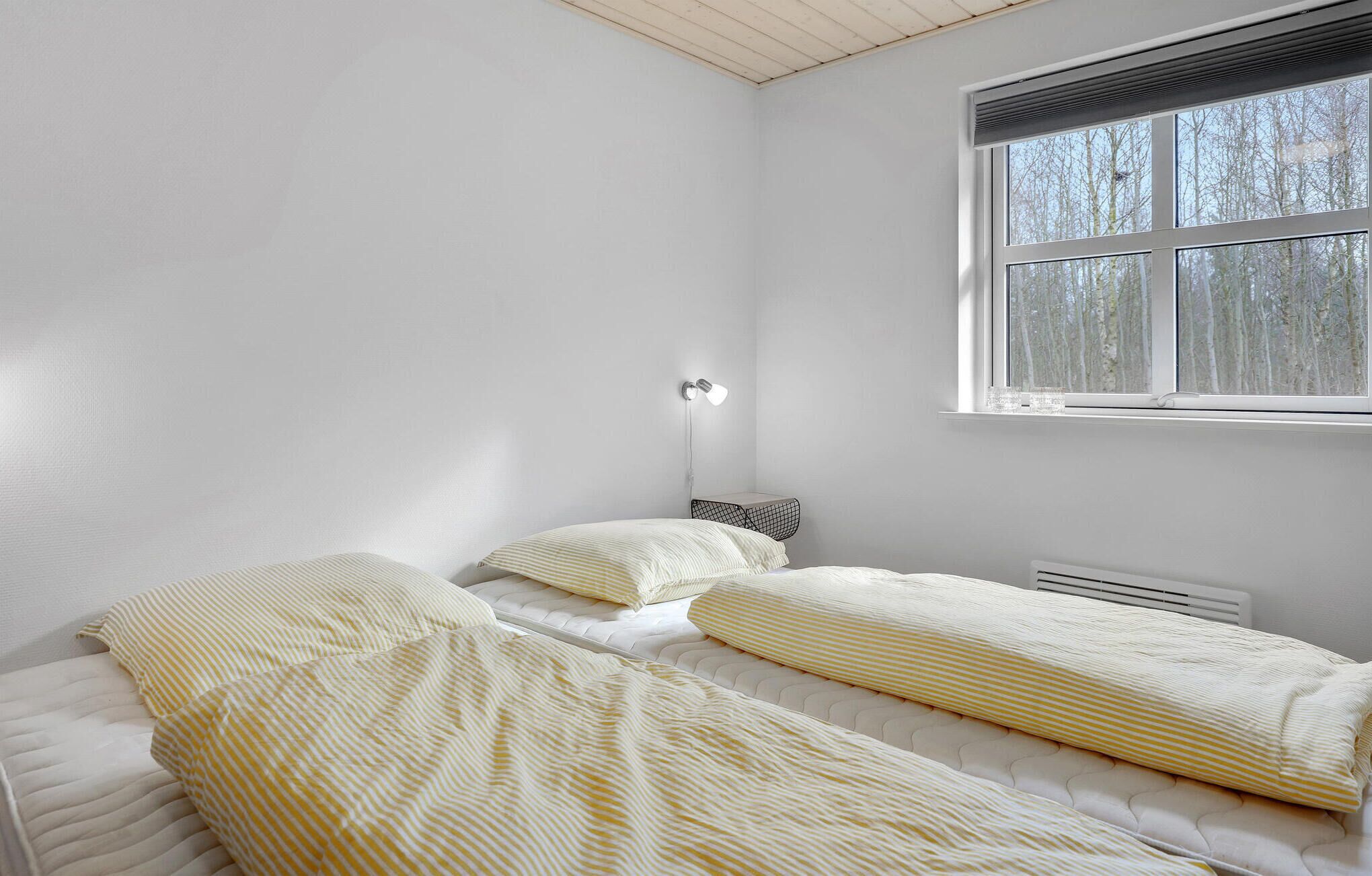 A bedroom with two beds, a window, and a wall-mounted lamp.