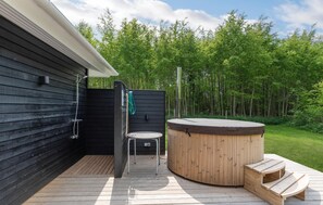 A wooden deck with a hot tub, a shower, and a chair.