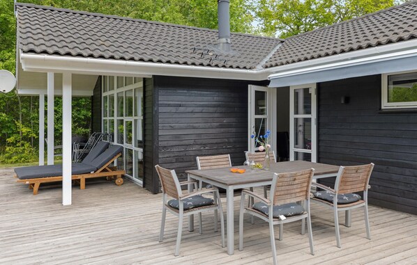 A covered outdoor patio with a table and chairs, a lounge chair, and a grill.