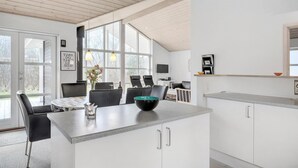Uma cozinha moderna com uma ilha grande, armários brancos e uma área de jantar com cadeiras pretas.