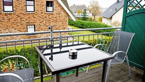 A balcony with a table and chairs, a brick building in the background, and a green gate. - Apartment with Balcony - Ferienhaus Alt-Baabe (Baabe)