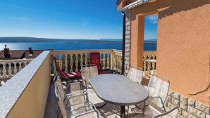 Un balcone con tavolo e sedie, affacciato su uno specchio d'acqua e la costa in lontananza.