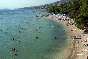 Una playa con aguas cristalinas, gente nadando y tomando el sol, y una hilera de árboles en la orilla.