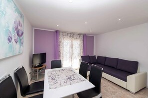 Una sala de estar moderna con una mesa blanca, sillas negras, un sofá púrpura y un televisor de pantalla plana.