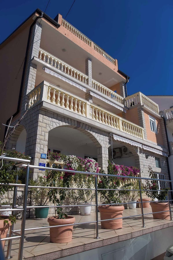 A two-story building with a balcony, potted plants, and a clear blue sky.
