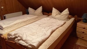 Una cama doble con ropa de cama blanca en una habitación de madera con techo inclinado.