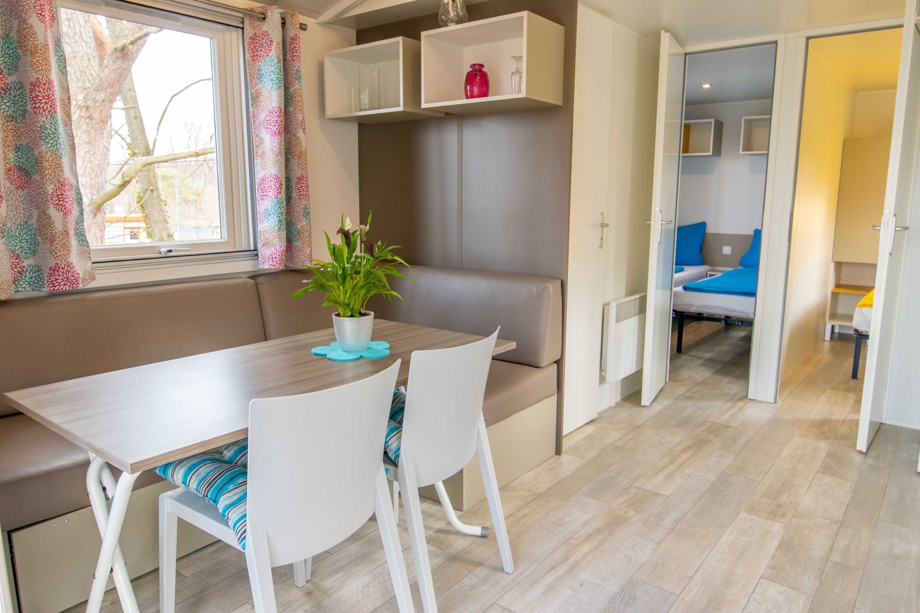 A modern, compact living space with a dining area, a sofa, a small kitchen, and a bedroom with a bed and a nightstand.