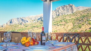 An outdoor dining area with a table set for two, featuring a bottle of wine, fruit, and glasses. The table is set against a backdrop of a mountainous landscape. - Gorgeous home in Alora-El Chorro (Alora-El Chorro)