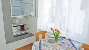 Avoin jääkaappi, jonka hyllyt ovat selkeästi näkyvissä, punainen kahvinkeitin ja pöytä, jonka päällä on kukkakuviollinen pöytäliina.