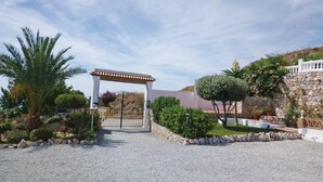 Un camino de grava conduce a una entrada con portón, una pérgola y un muro de piedra.