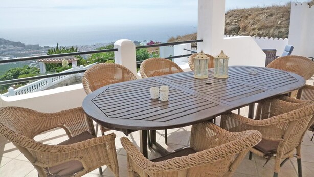 Un área de comedor al aire libre con sillas de mimbre y una mesa redonda, con vistas a un paisaje pintoresco.