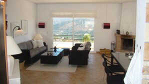 Un salón con sofá, sillones, una mesa de centro y chimenea. Hay un ventanal con vistas a un paisaje montañoso.