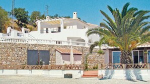 Un edificio de dos pisos con fachada de piedra, un balcón y una palmera en primer plano.
