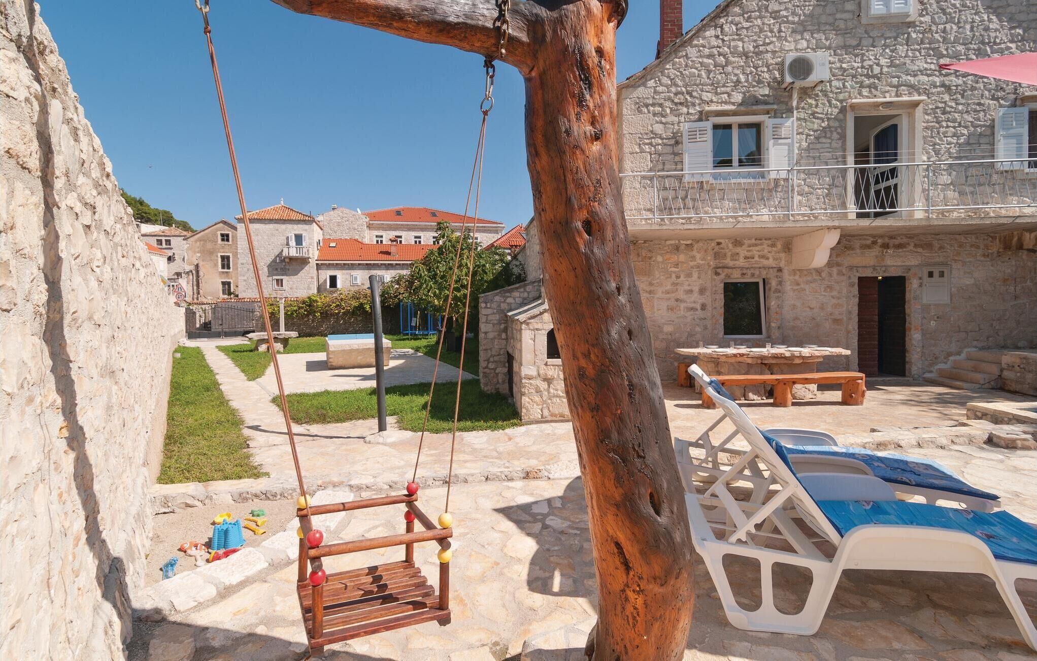 A stone building with a balcony, a swing set, and a pool area with lounge chairs.