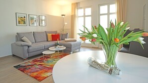 Ein modernes Wohnzimmer mit einem grauen Sofa, einem runden Couchtisch und einer Blumenvase.