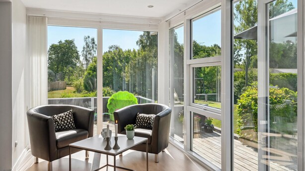 A modern room with two leather armchairs, a small table, and a large window offering a view of a garden and trees. - Amazing home in Rudkøbing with WiFi (Rudkøbing)