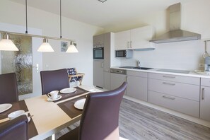 A modern kitchen with a microwave, oven, and stainless steel range hood. There is a dining table with chairs and a decorative item on the wall.