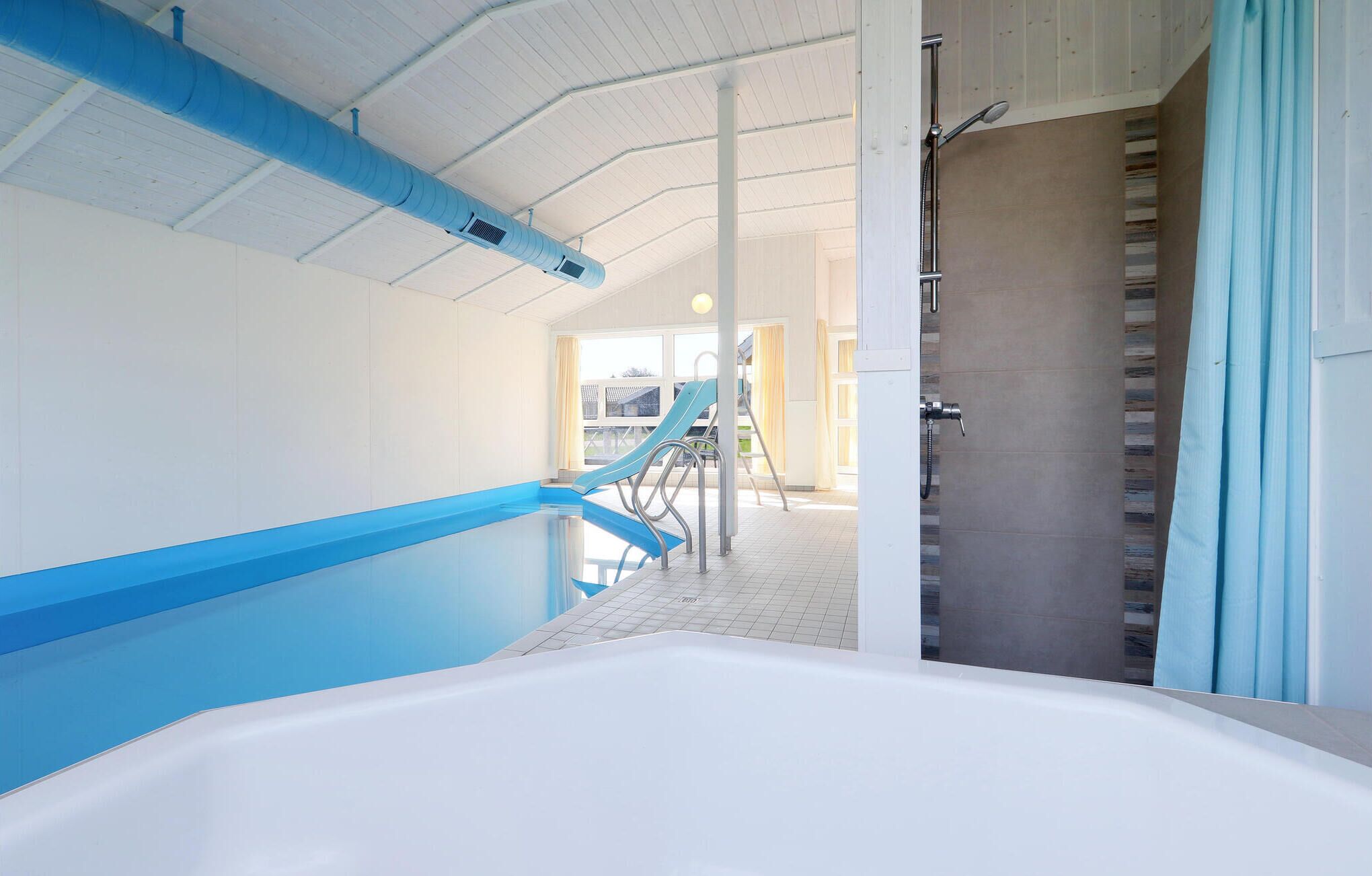 Uma área de piscina com esquema de cores azul e branco, espaço para chuveiro e vista para o exterior.