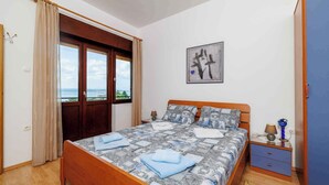 Un dormitorio con cama de madera, vistas a través de un ventanal grande, una mesita de noche con lámpara y un armario azul.
