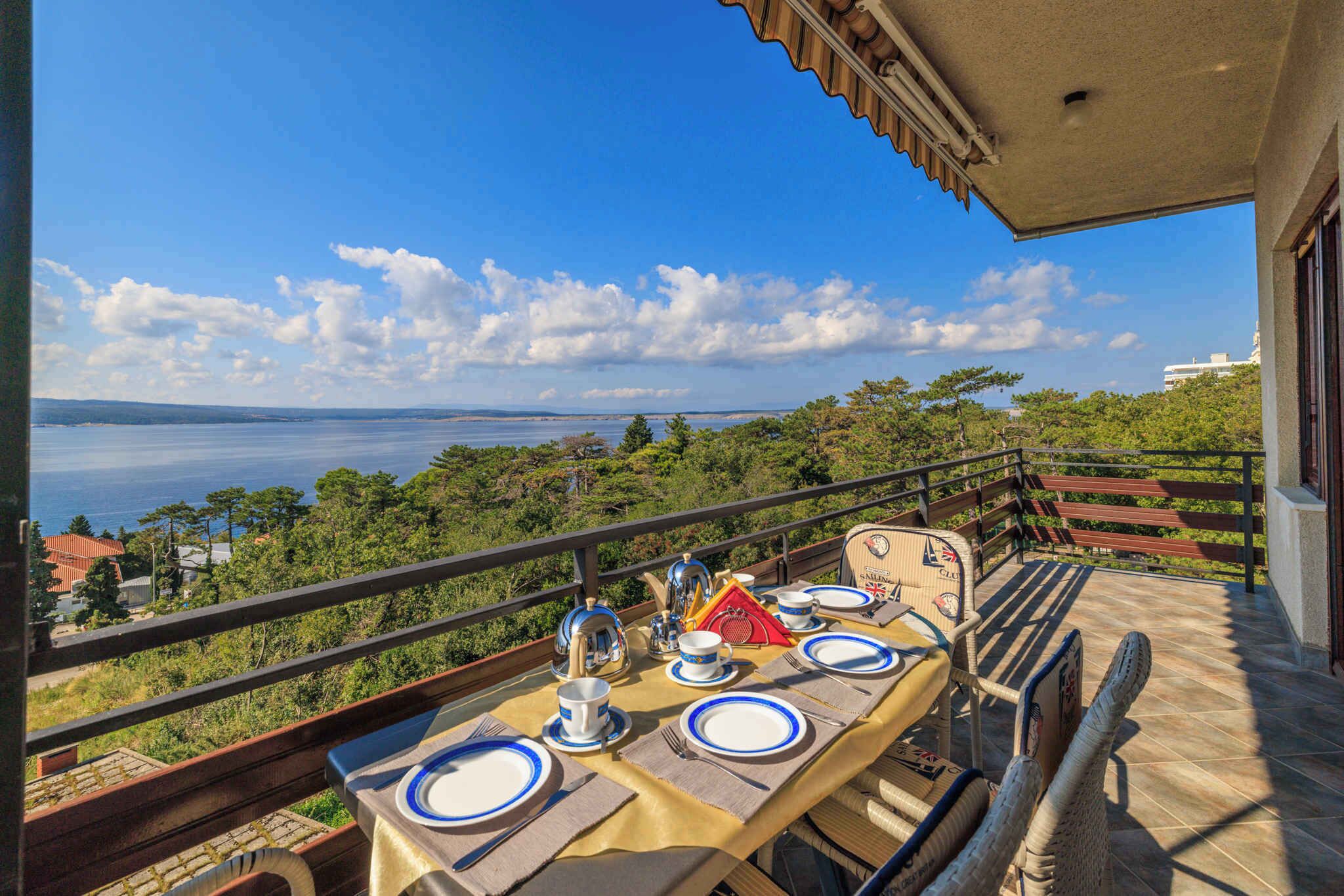A table set for dining on a balcony with a scenic view of the sea and hills.