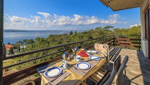 Una mesa preparada para comer en un balcón con vistas panorámicas al mar y colinas.