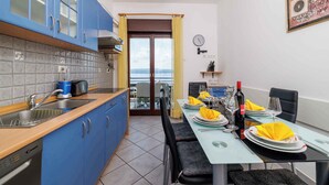Cocina moderna con armarios azules, lavavajillas y comedor para cuatro, con servilletas amarillas y copas de vino.