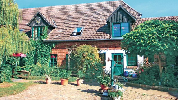 Une maison traditionnelle avec un toit en tuiles, des murs en briques et un jardin agrémenté de plantes en pot.
