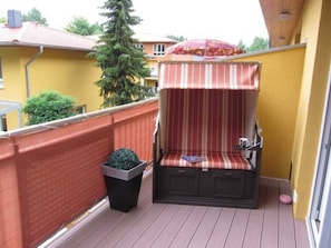 Un balcon avec un auvent rayé, une petite plante en pot et une poubelle.