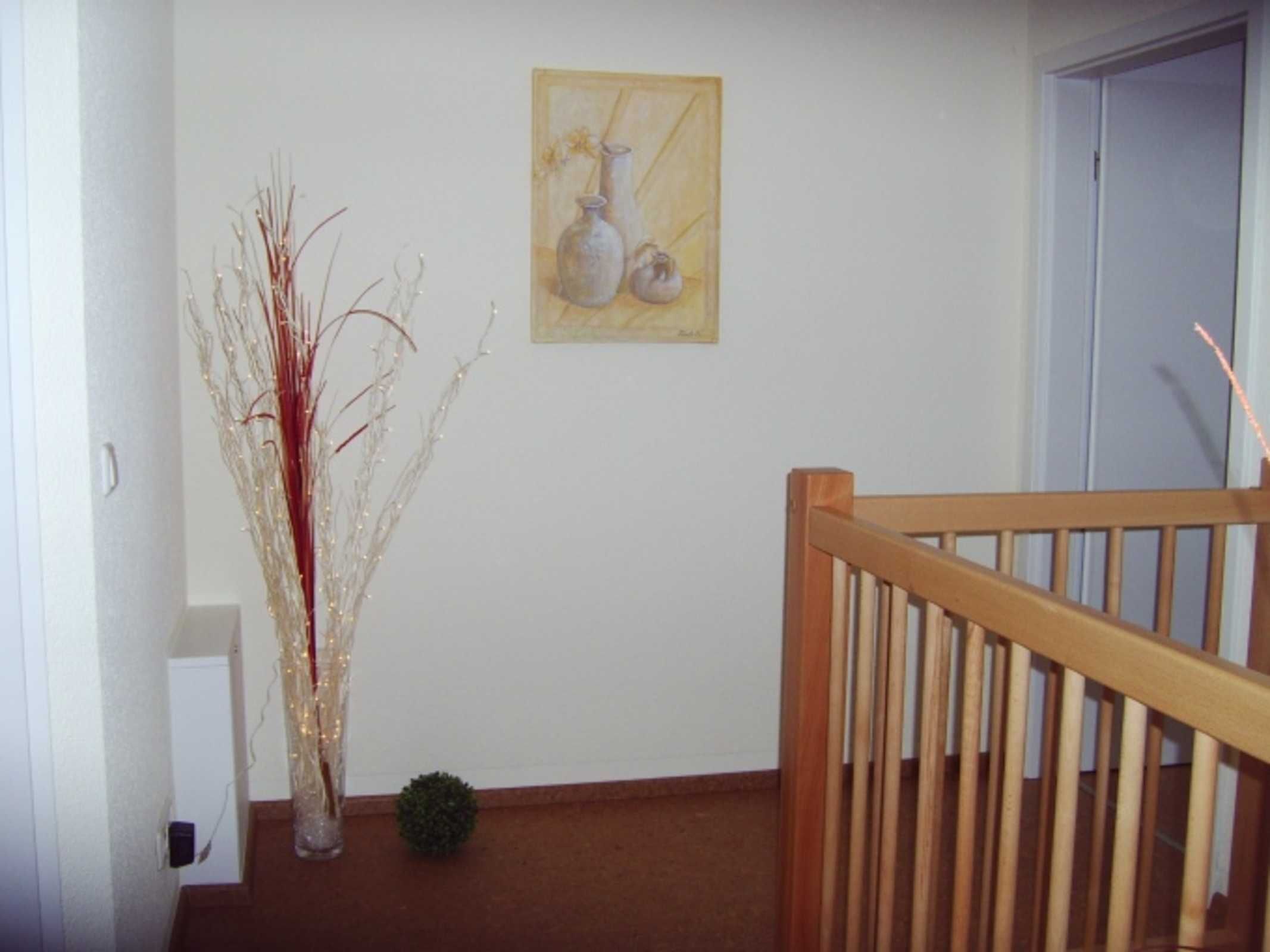 Ein Flur mit Holzbalkon, einer Vase mit Zweigen und einem Bild an der Wand.