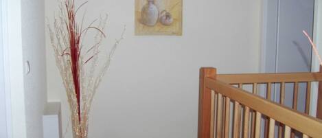 Ein Flur mit Holzbalkon, einer Vase mit Zweigen und einem Bild an der Wand.